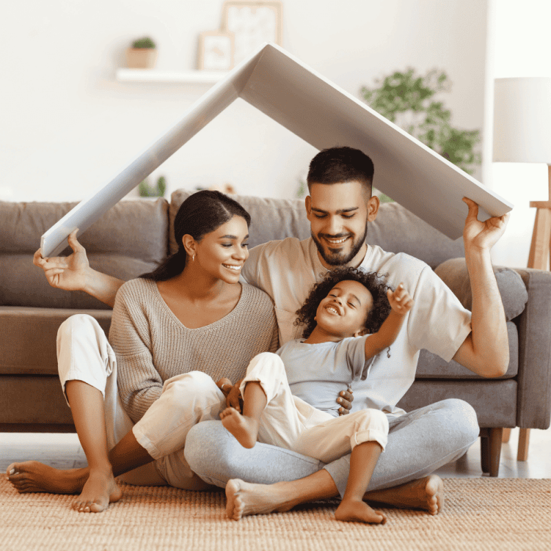 A smiling family sitting on the living room floor while parents hold a stylized roof cutout over their daughter in an Orlando home.