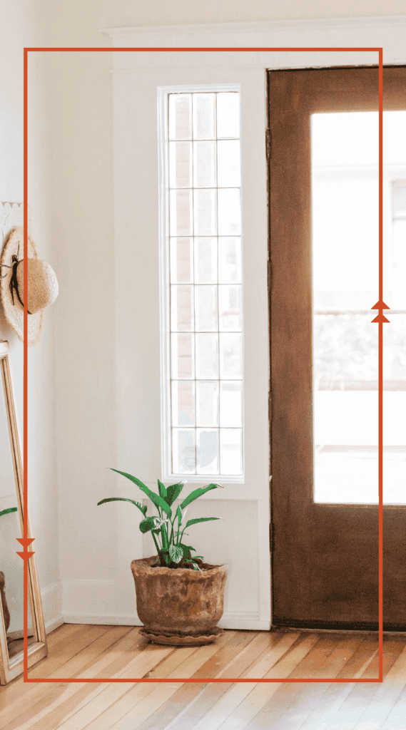 Bright home entryway with a wooden front door, tall window and potted plant on a hardwood floor
