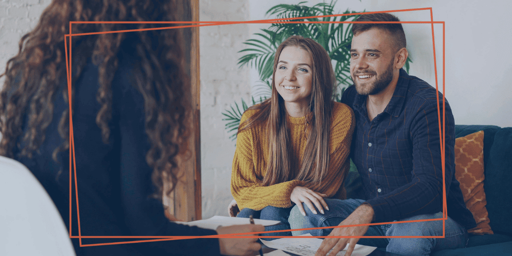 Smiling couple on a couch listening to an advisor holding paperwork