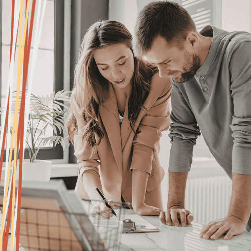 Young couple leaning over a desk reviewing paperwork together, the woman writing with a pen