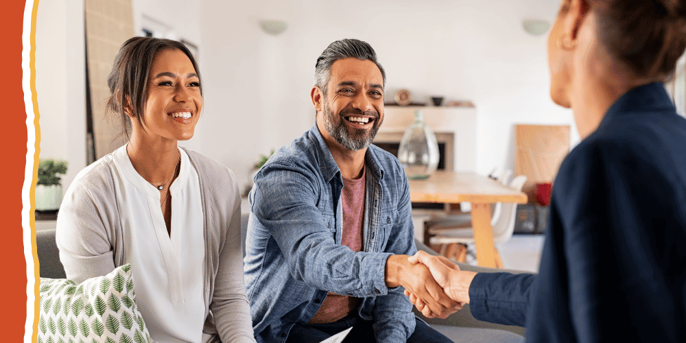 Smiling couple on a couch, the man shaking hands with a woman across from them