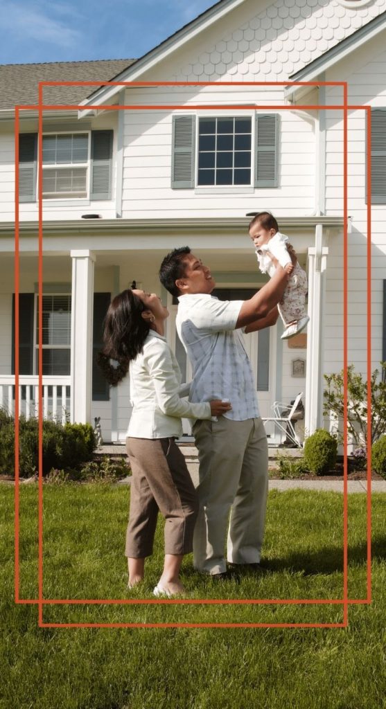 Young family celebrating on the front lawn of their two-story home, father lifting their baby overhead