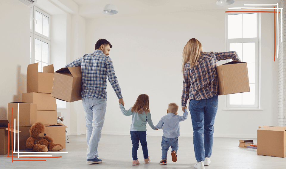 Family carrying moving boxes into an empty home, parents holding hands with their two young children