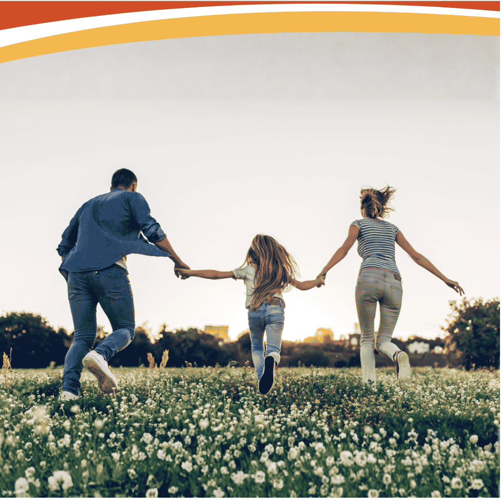 Family holding hands running through a field of white wildflowers at sunset, buildings on the horizon