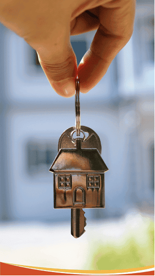 Hand holding a house-shaped key on a key ring in front of a blurred building