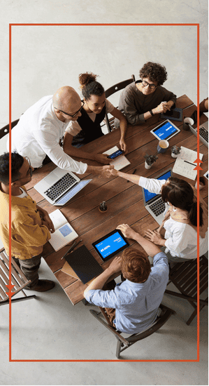 Overhead view of a team meeting around a wooden table with laptops and tablets, two people shaking hands