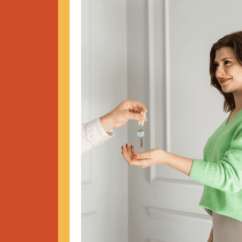 Smiling woman in a green cardigan holding out her hand to receive a set of keys in front of a white door
