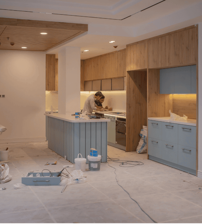 Two workers at the counter of a modern kitchen under renovation, with new wood and pale blue cabinets